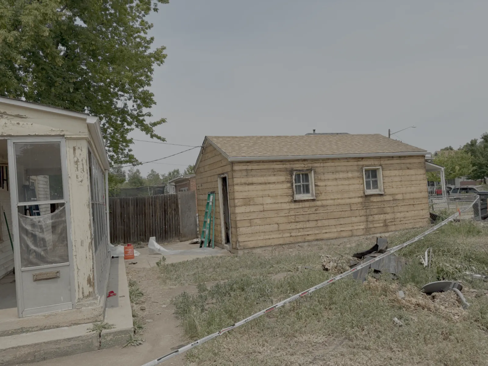 Backyard view of an outbuilding being abated of asbestos siding with caution tape perimeter, ladders and tools staged by Advantage Environmental