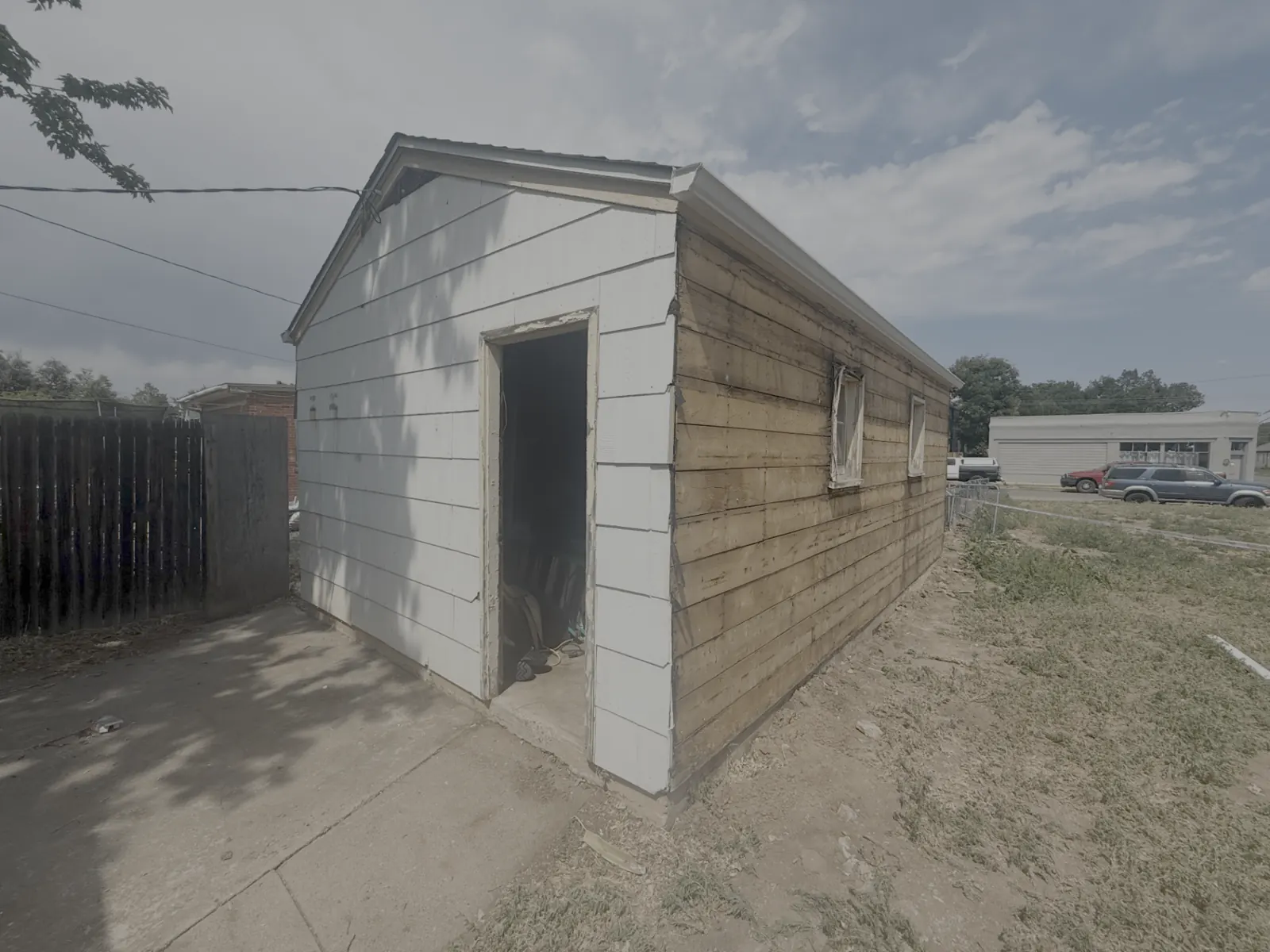 Detached garage stripped of asbestos-containing exterior siding boards exposing original wood sheathing, mid-abatement by AHERA-certified Denver crew
