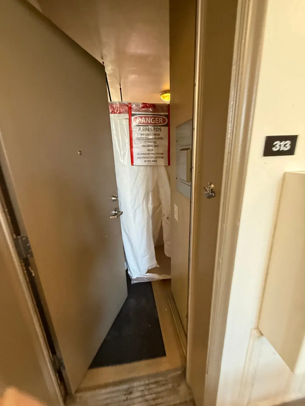 Sealed poly containment entry with a DANGER ASBESTOS warning sign at a Denver apartment bathroom abatement