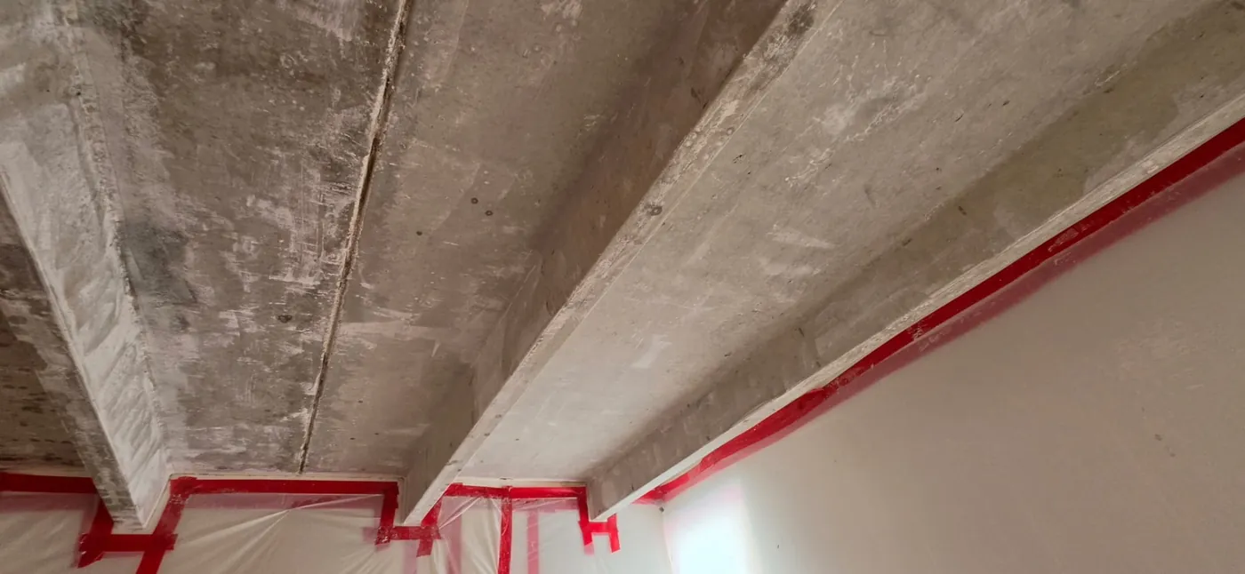 Popcorn ceiling texture fully scraped off exposing the bare concrete deck and beams inside a taped Denver containment